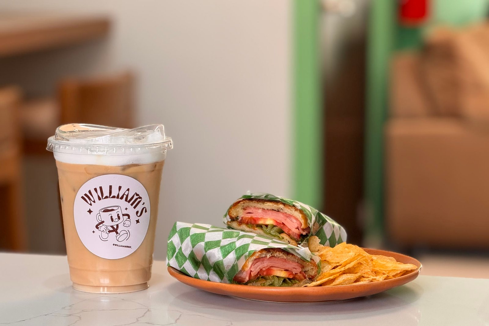 Torta caliente de jamón, queso y jitomate con papas, junto a un café frío de Williams.