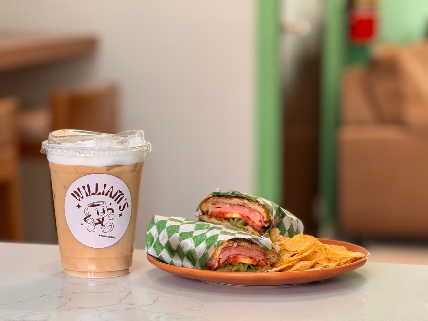 Torta caliente de jamón y queso con papas, junto a un café frío de Williams.