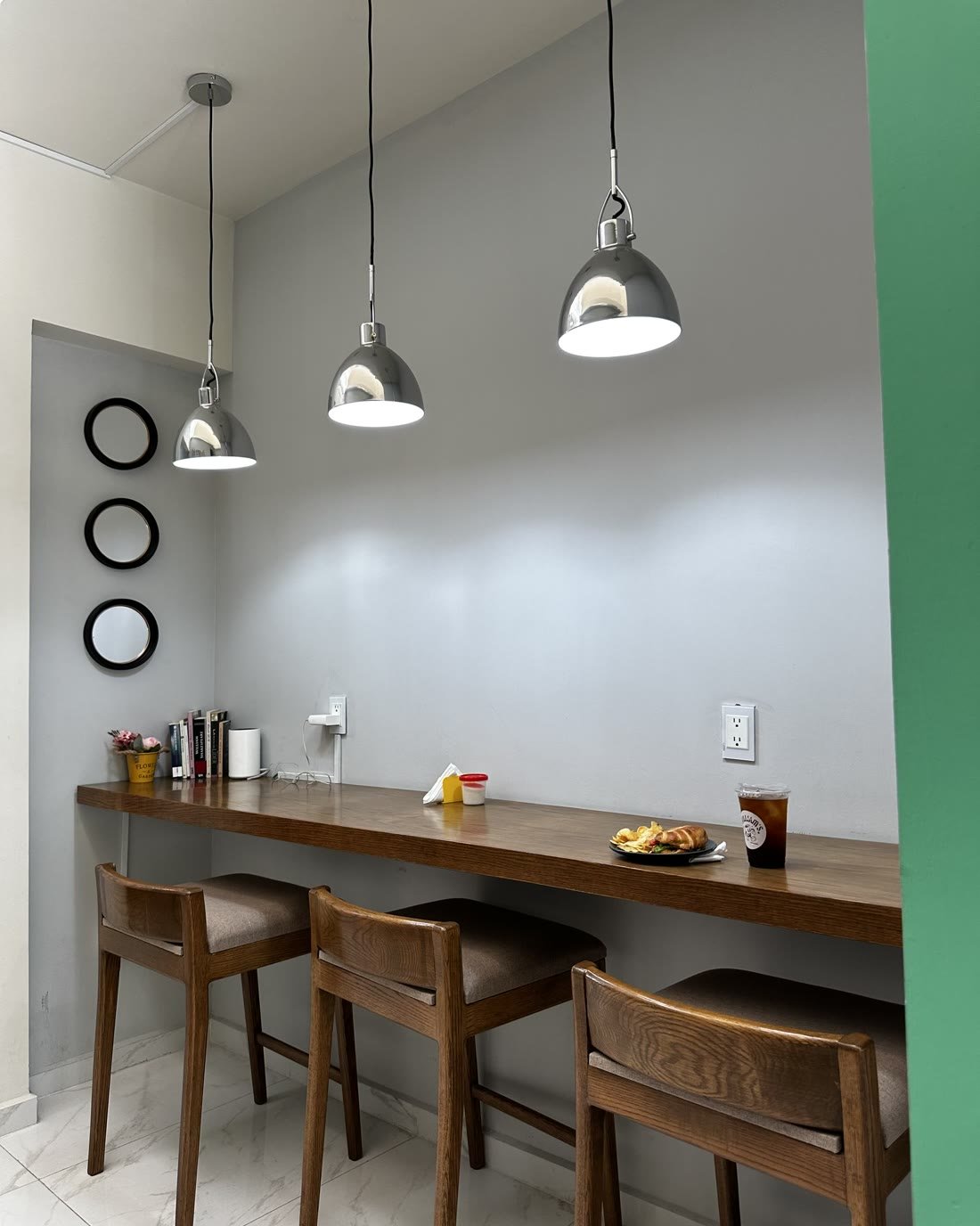 La barra larga de madera con banquetas y lámparas colgantes, para sentarse a esperar.